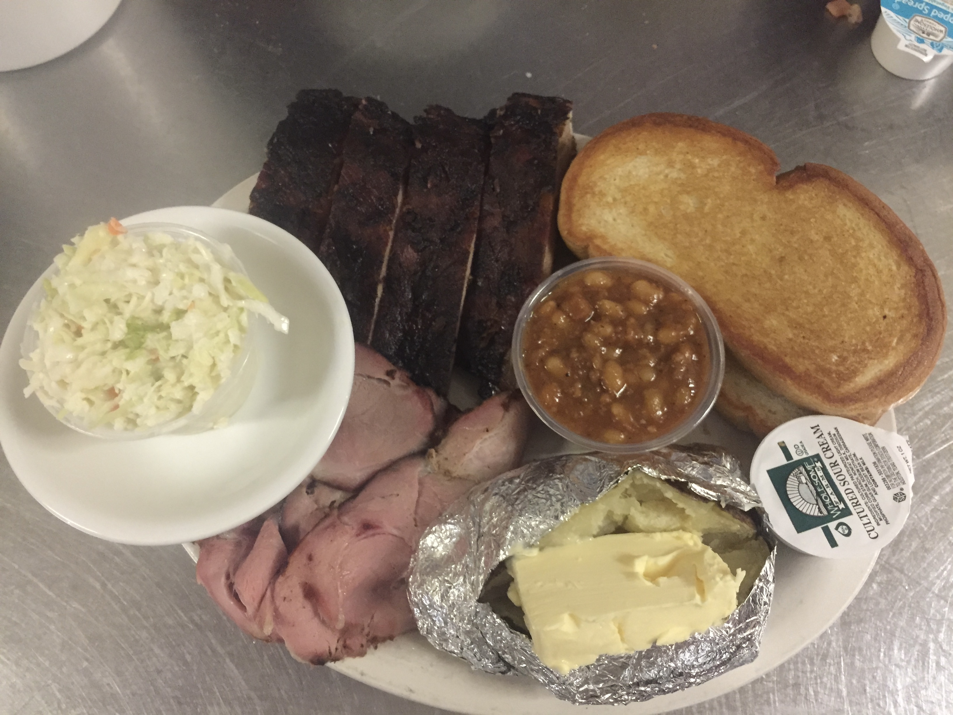 Sliced Pork and St. Louis Ribs shown served with Baked Potato with butter,  BBQ Beans, Coleslaw, and Garlic Bread